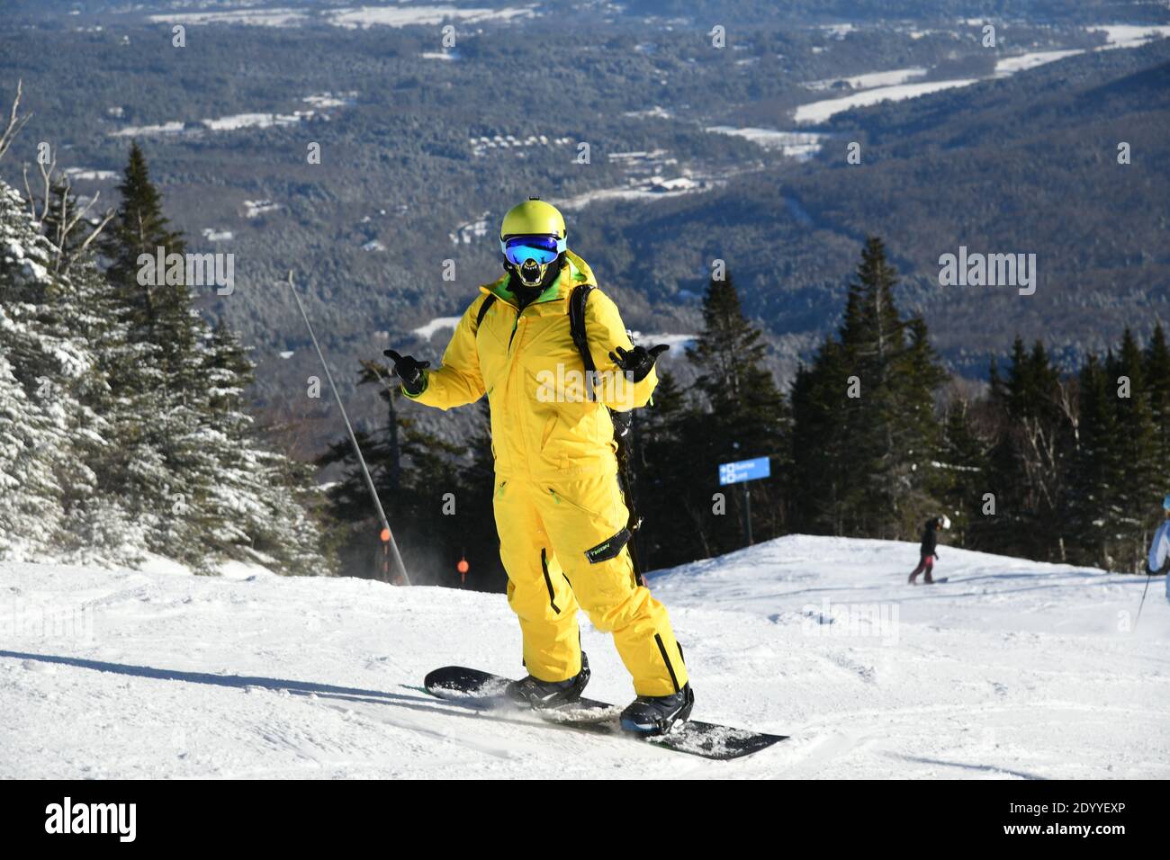 Snowboarder riding down the slopes wearing yellow mono suit on sunny day with fresh snow. Stowe mountain ski resort, VT 2020. Hi resolution image Stock Photo
