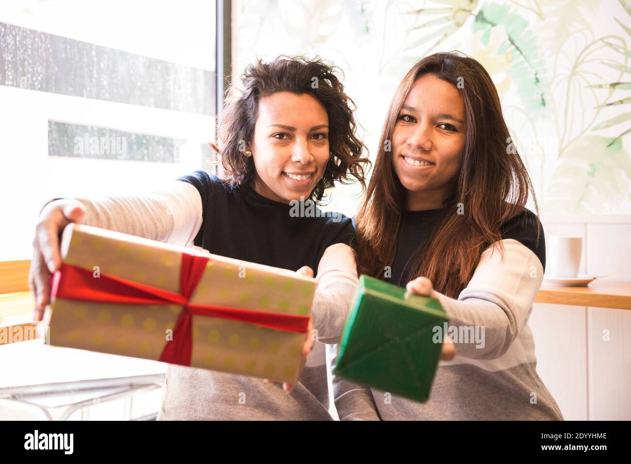 Two smiling latin girls showing off a present. They are inside a coffee shop. Stock Photo