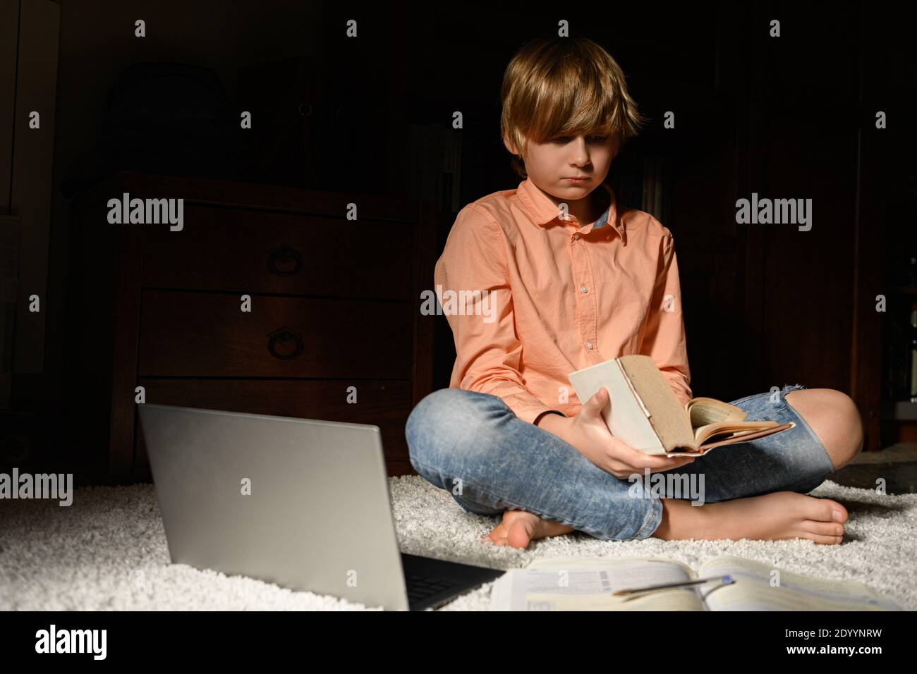 A boy reading a book, sitting on the floor near the laptop Stock Photo ...