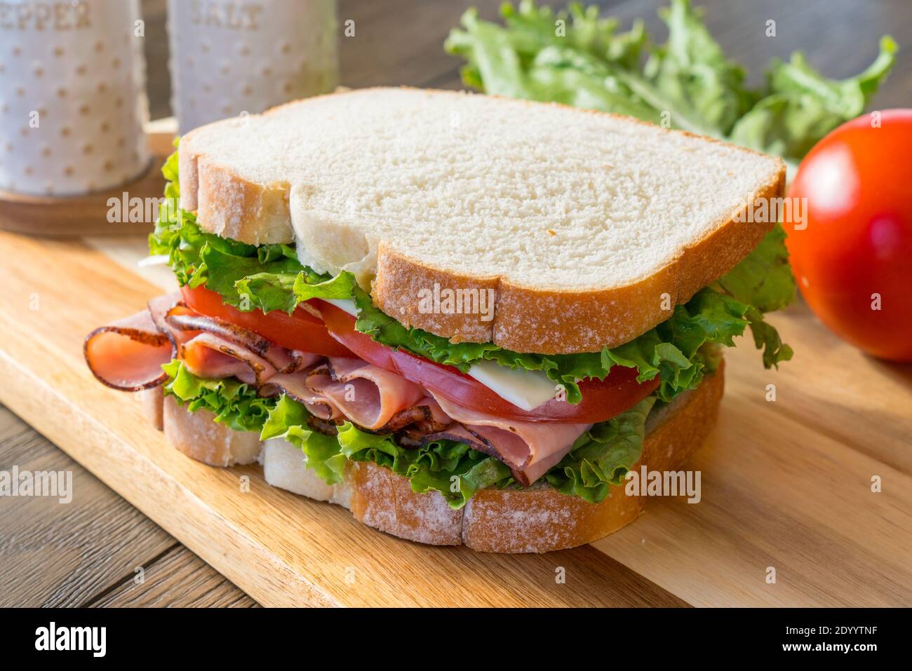 Fresh ham, tomato and cheese sandwich on cutting board Stock Photo