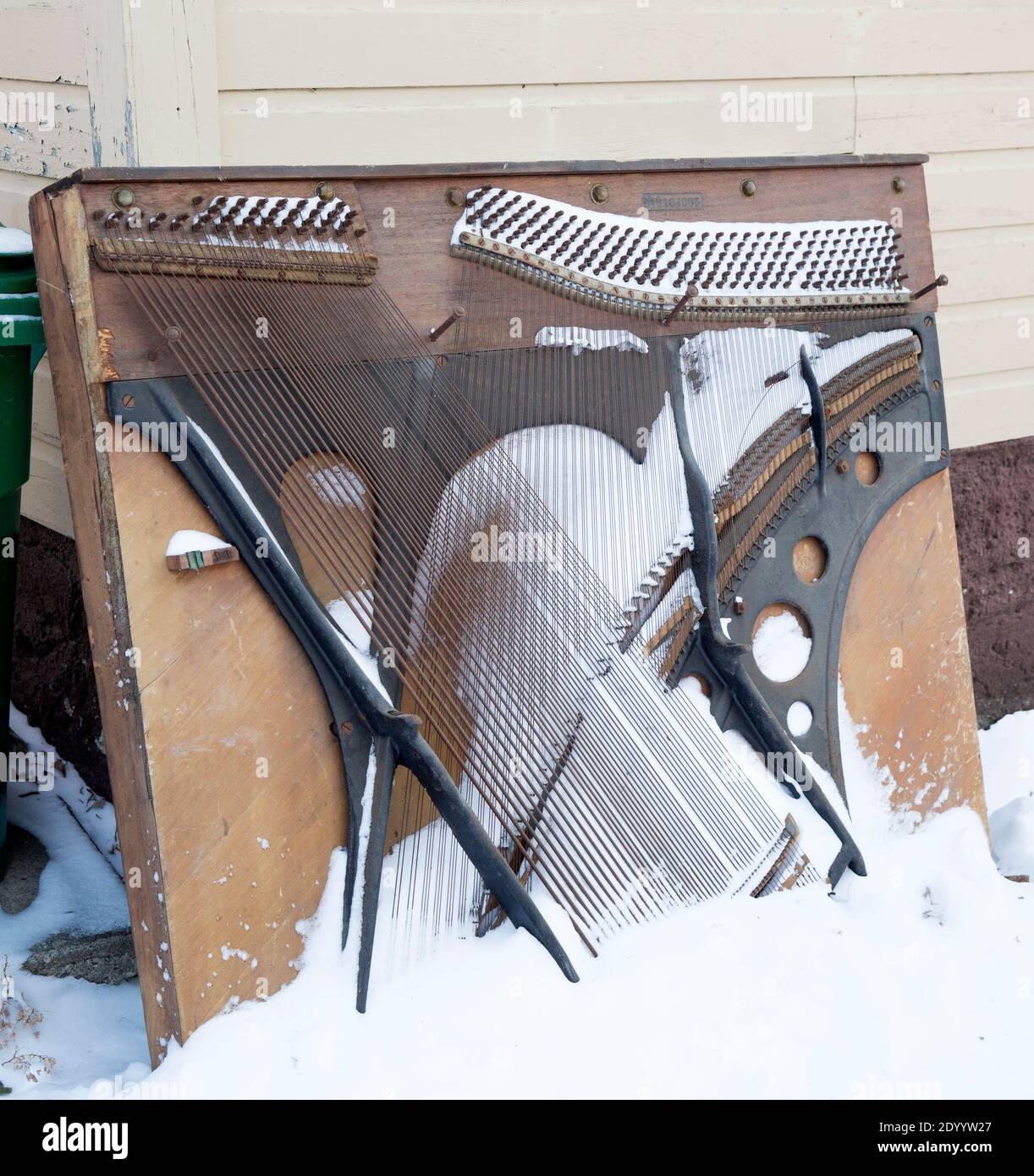 Snow covered old vintage upright piano soundboard in the alley awaiting garbage and solid waste removal Stock Photo