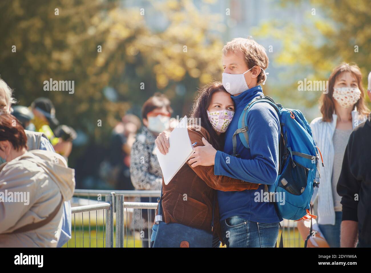 Embracing couple in love with home-made cloth face masks waiting in line of people for collective immunity test against corona virus. Stock Photo