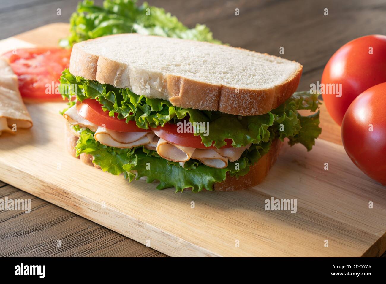 Fresh turkey, lettuce and tomato sandwich on cutting board Stock Photo