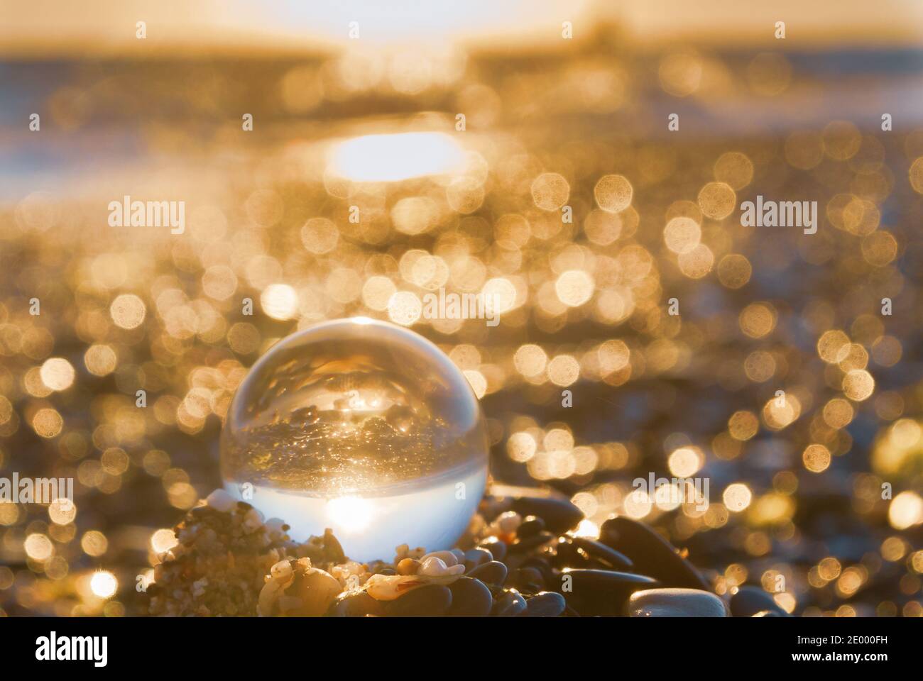 Glass round ball on the beach reflects the sea in summer at sunset ...