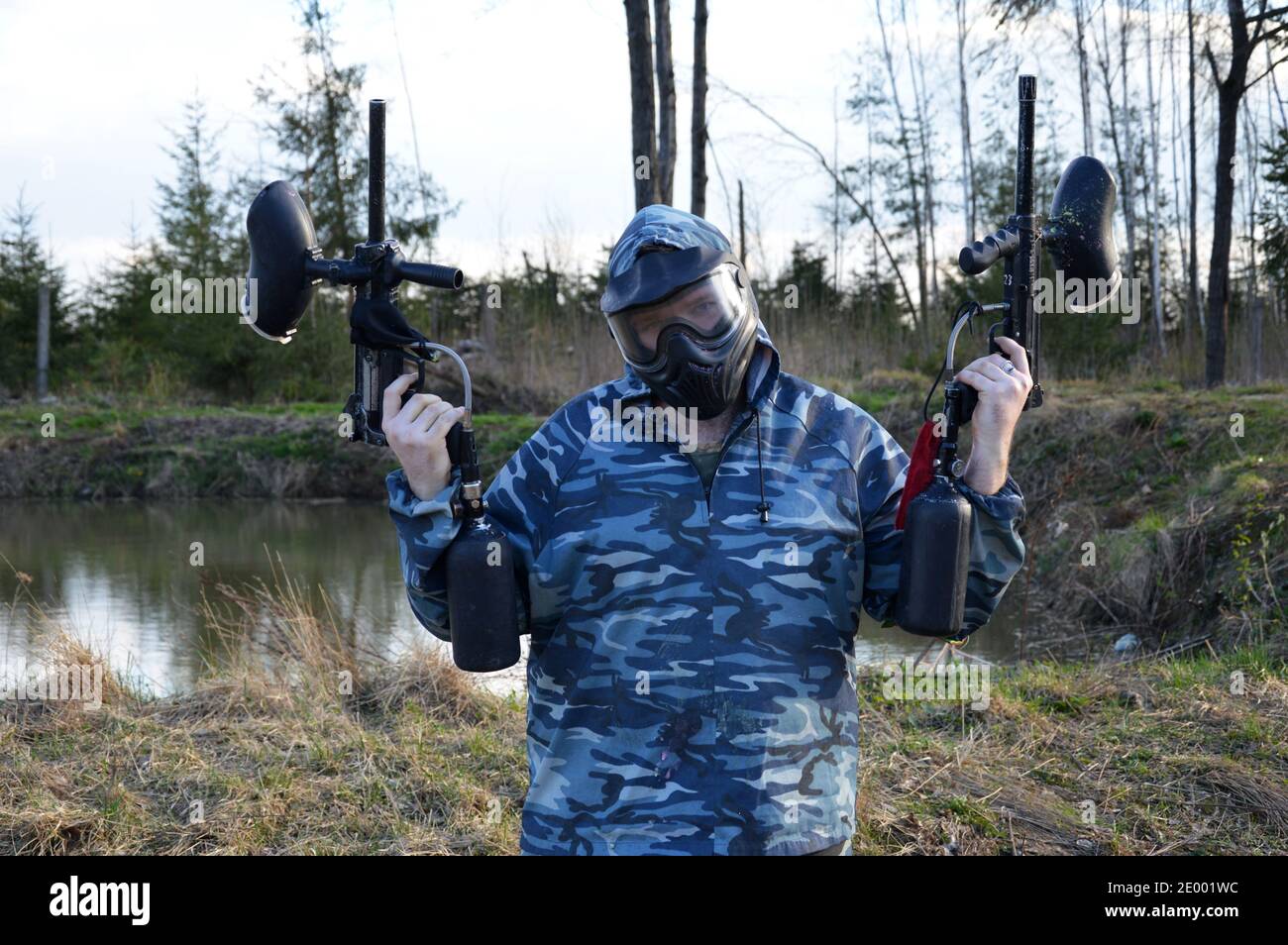 Man in camouflage clothing aiming a paintball guns. Boy in a protective