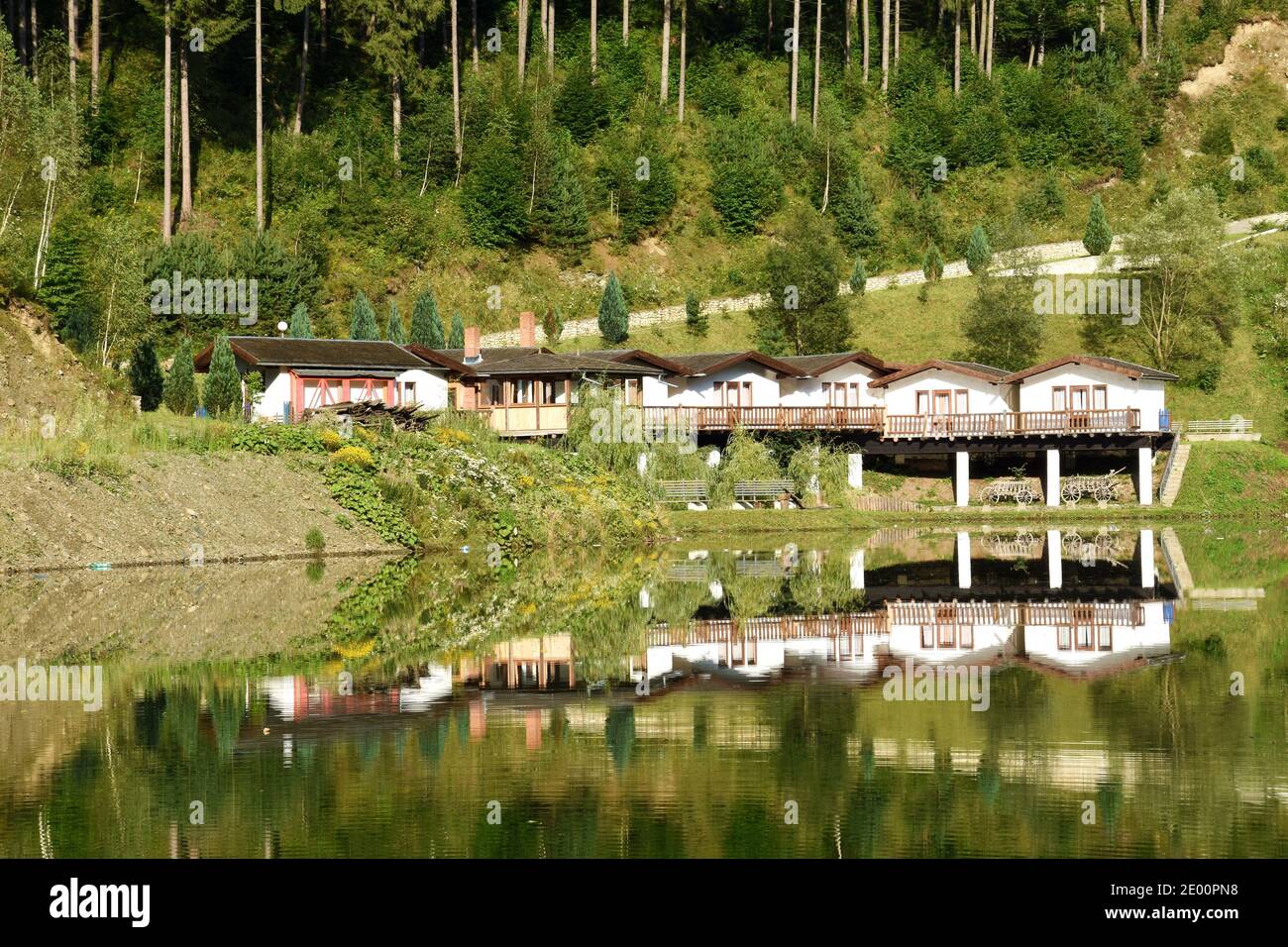 Landscape of an pension and green trees forest mirrored in the lake. Panorama reflection in the water. Stock Photo