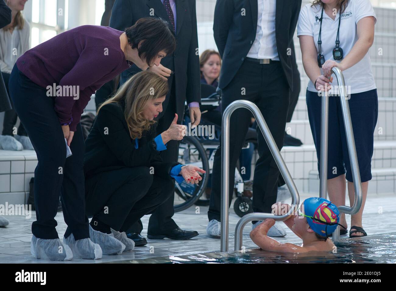 Companion of France's President Valerie Trierweiler and French Junior Minister for Disabled People Marie-Arlette Carlotti talk with next to Theo, a 13-year-old 4-limb amputee, standing in a pool, as part of their visit on November 27, 2013 in Vichy, central France. Theo is a grant holder of the disabled sports branch of the French Expertise and Performance Ressource Centre (CREPS) of Vichy Auvergne, where he trains in swimming. In early 2013, he competed for the first time in the French disabled swimming championships. At left is seen French Handisports Federation President Gerard Masson. Phot Stock Photo