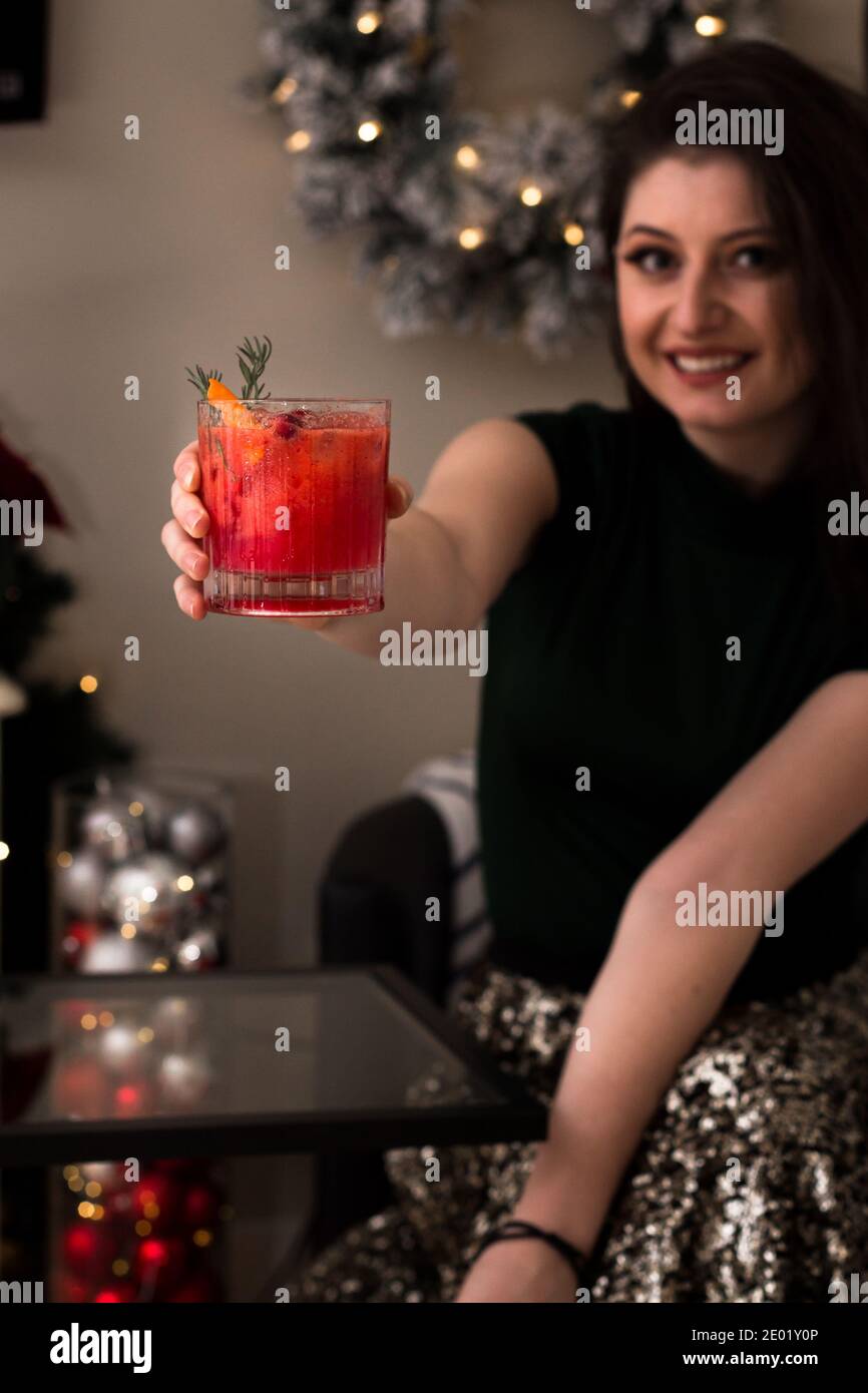 Pretty young woman holding up a delicious cranberry cocktail at Christmas. Stock Photo