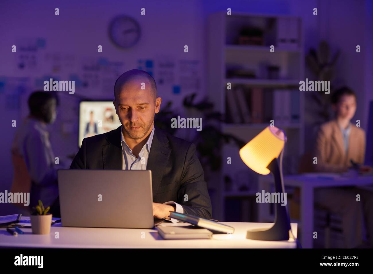Group of three modern office workers sitting at desks finishing workday late in evening, copy space Stock Photo