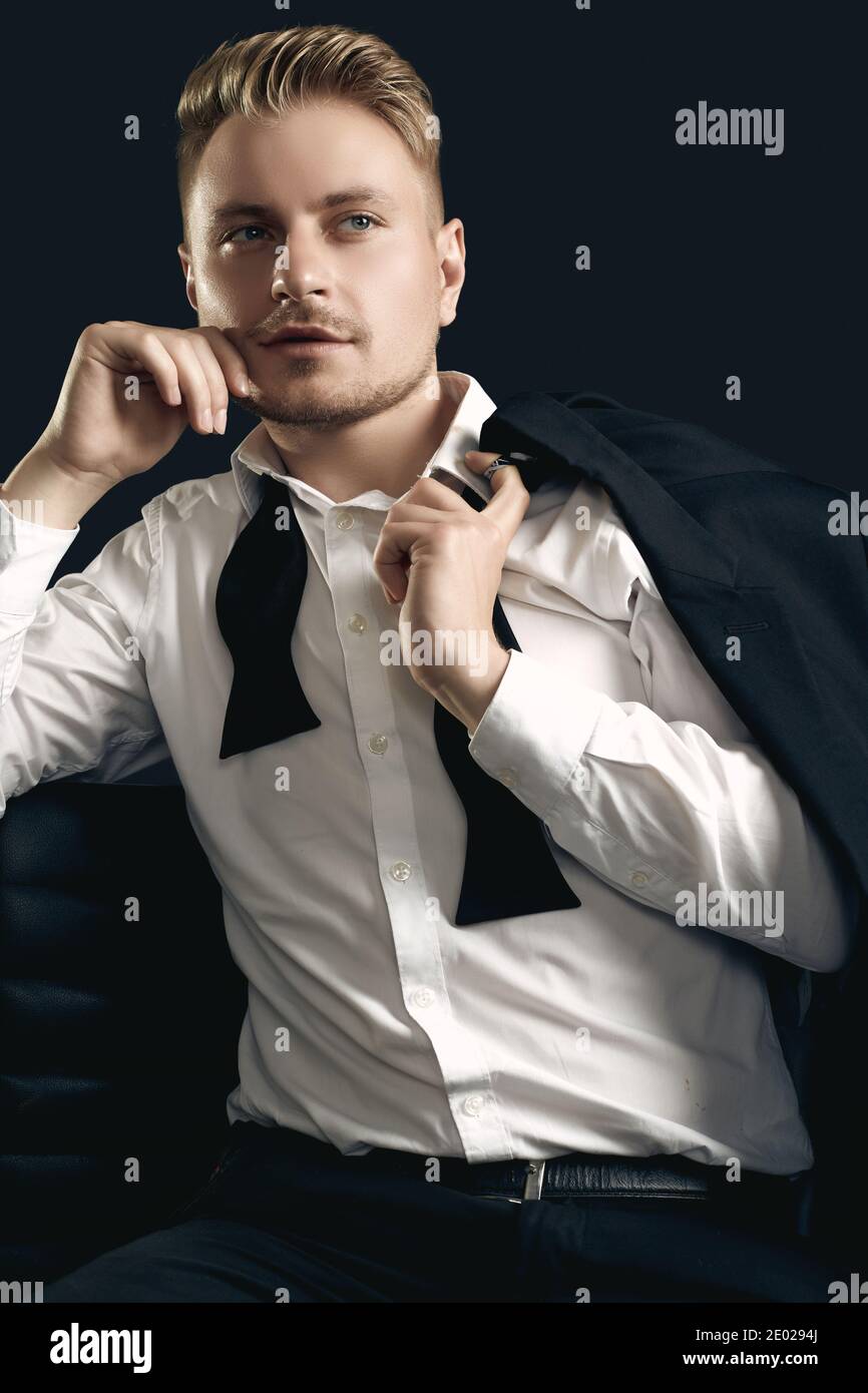 Portrait of handsome blond man in elegant tuxedo and bow tie posing on black studio background Stock Photo