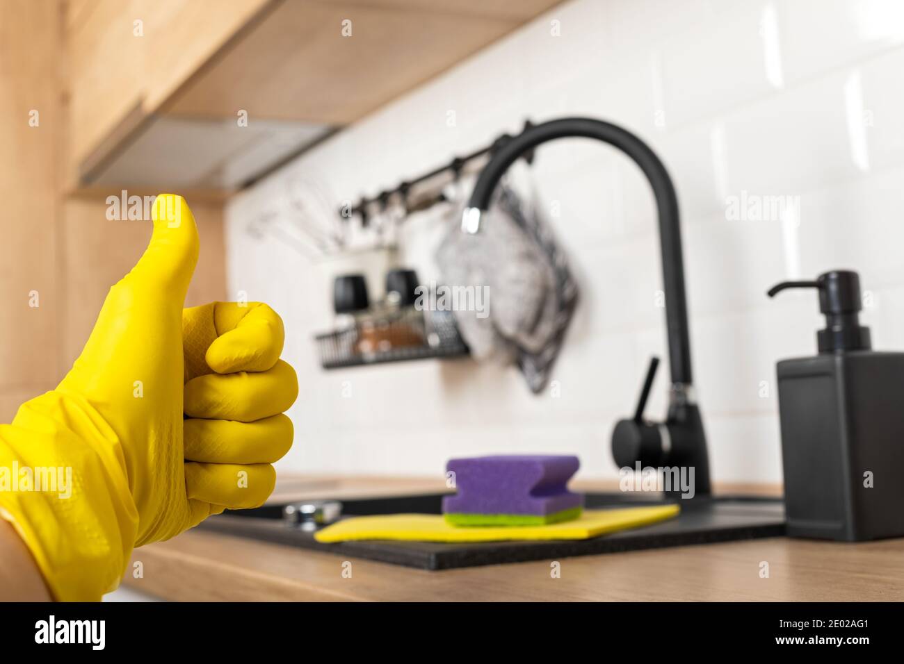 Housekeepers hand holding cleaning supplies in front of black kitchen