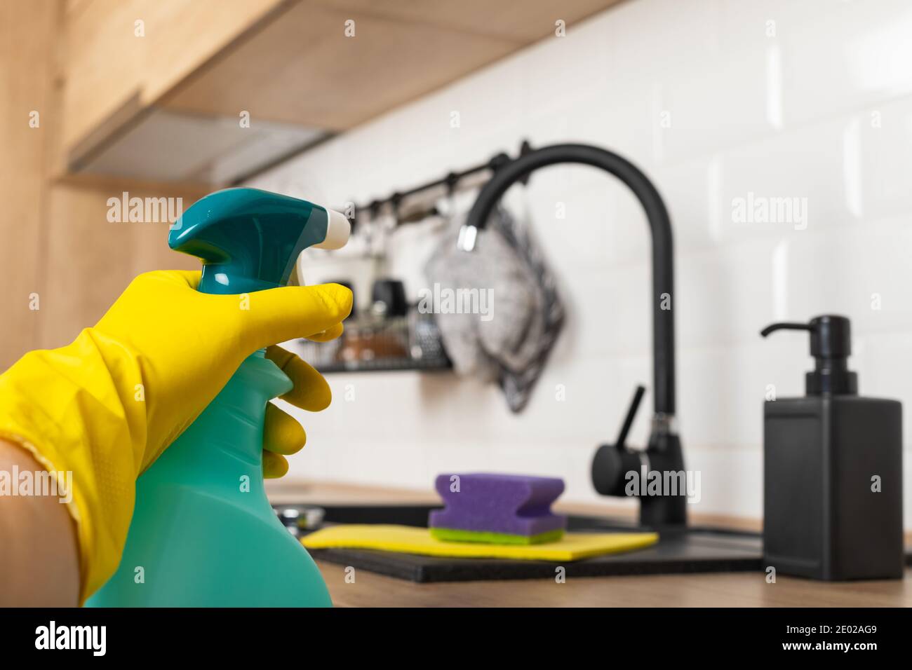Housekeepers hand holding cleaning supplies in front of black kitchen