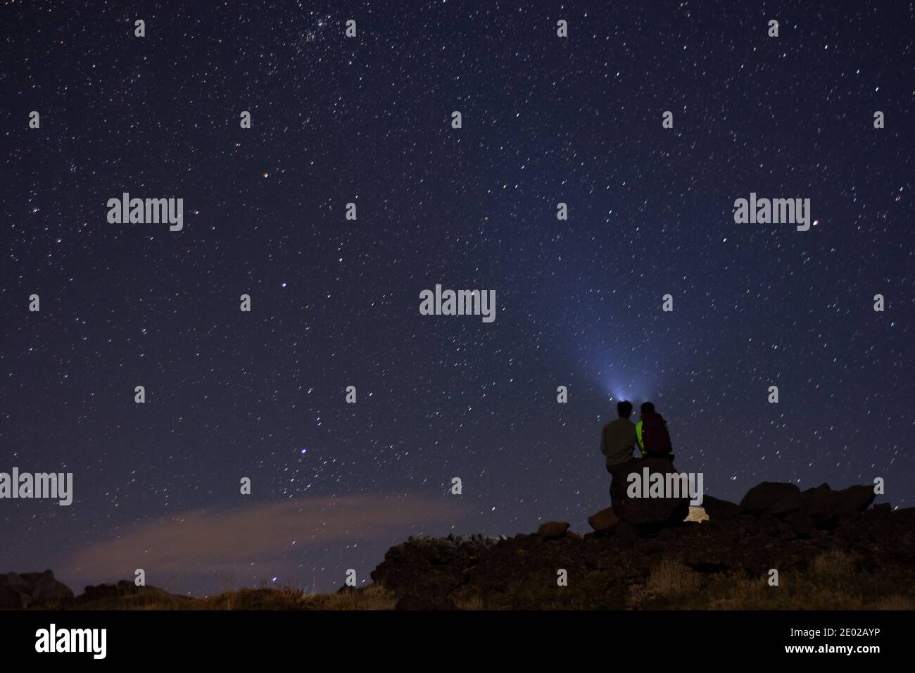 Couple hikes Thunder Mountain in the dead of night, they gaze into the stars Stock Photo