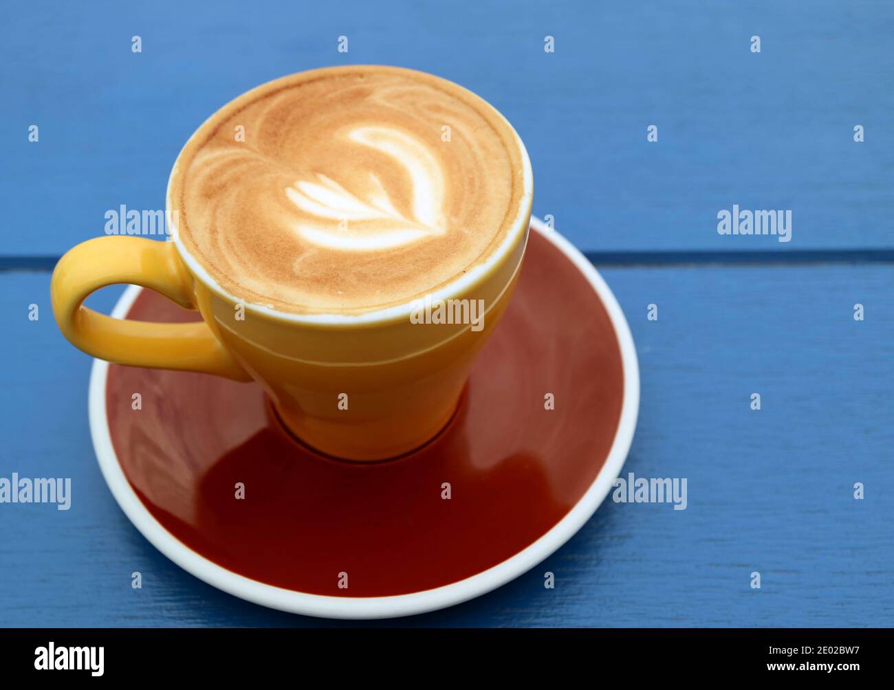 Closeup of cappuccino coffee in yellow brown cup isolated on blue wooden table Stock Photo