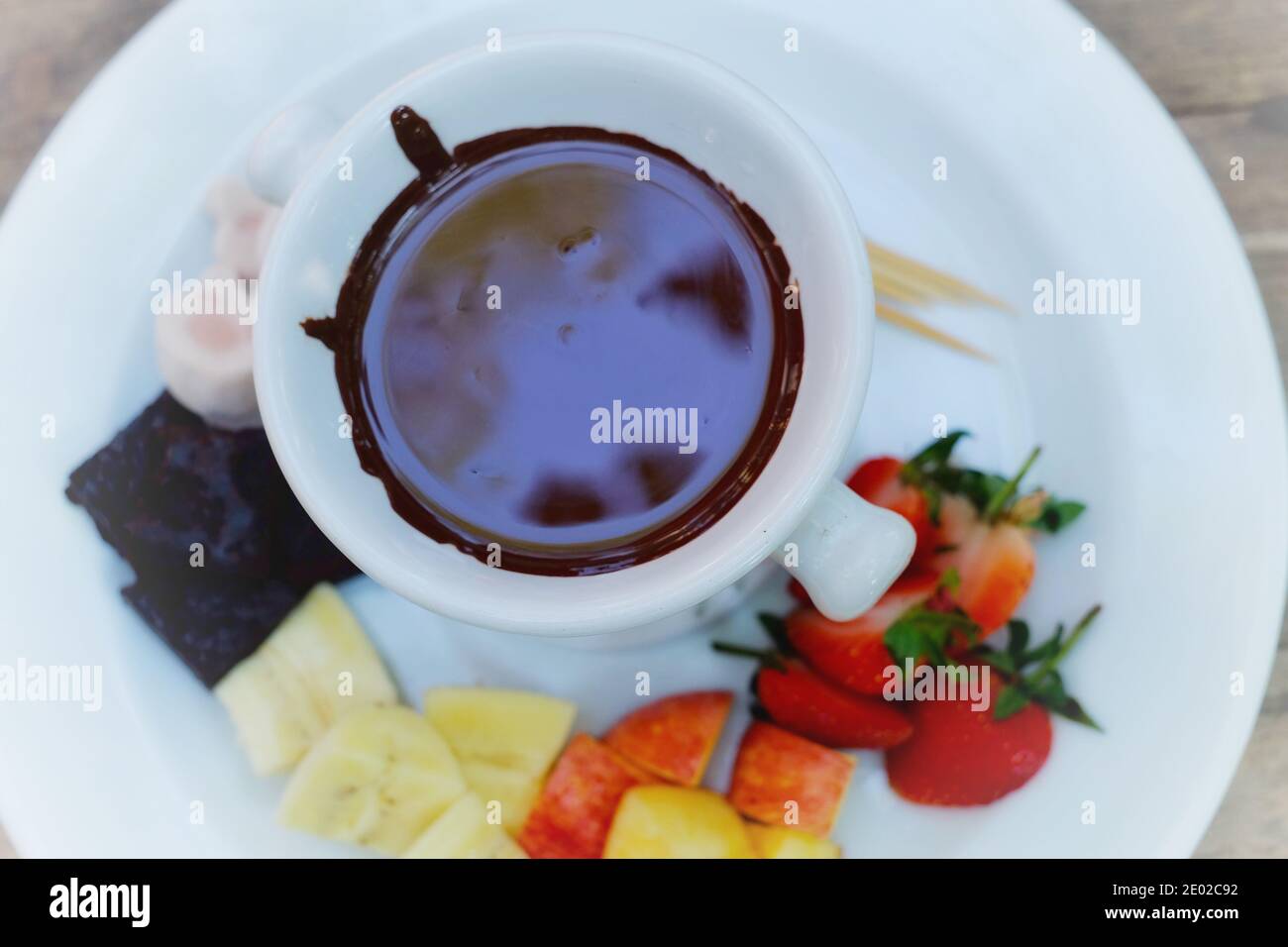 The top view of a set of chocolate fondue with fruits and cakes and toothpick for dipping into hot chocolate with white dish and pot. Stock Photo
