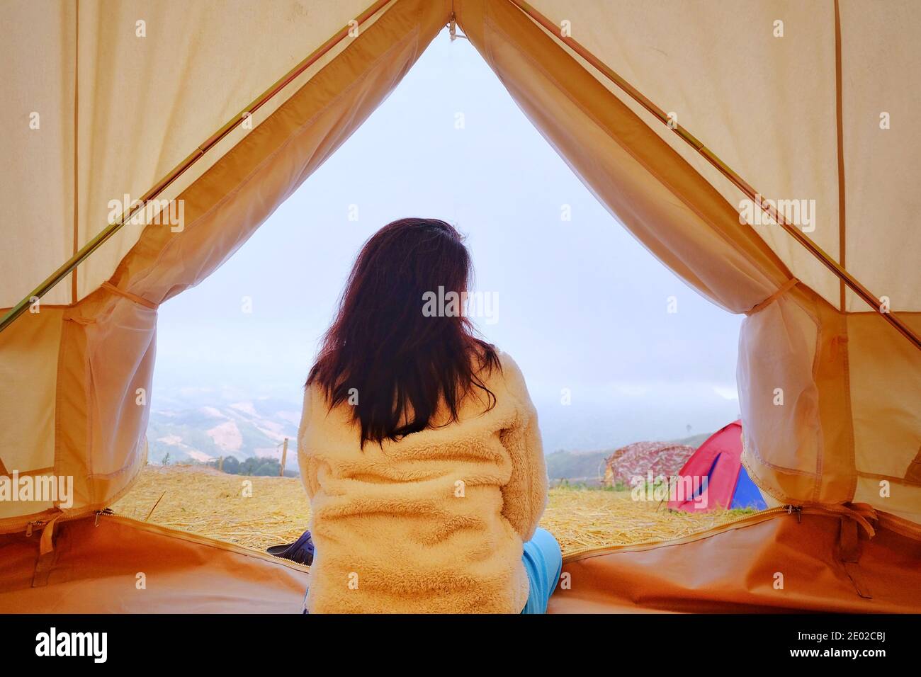 A young woman sitting peacefully at inside her white tent in the morning with cool breeze and morning sun, stretching and relaxing. Stock Photo