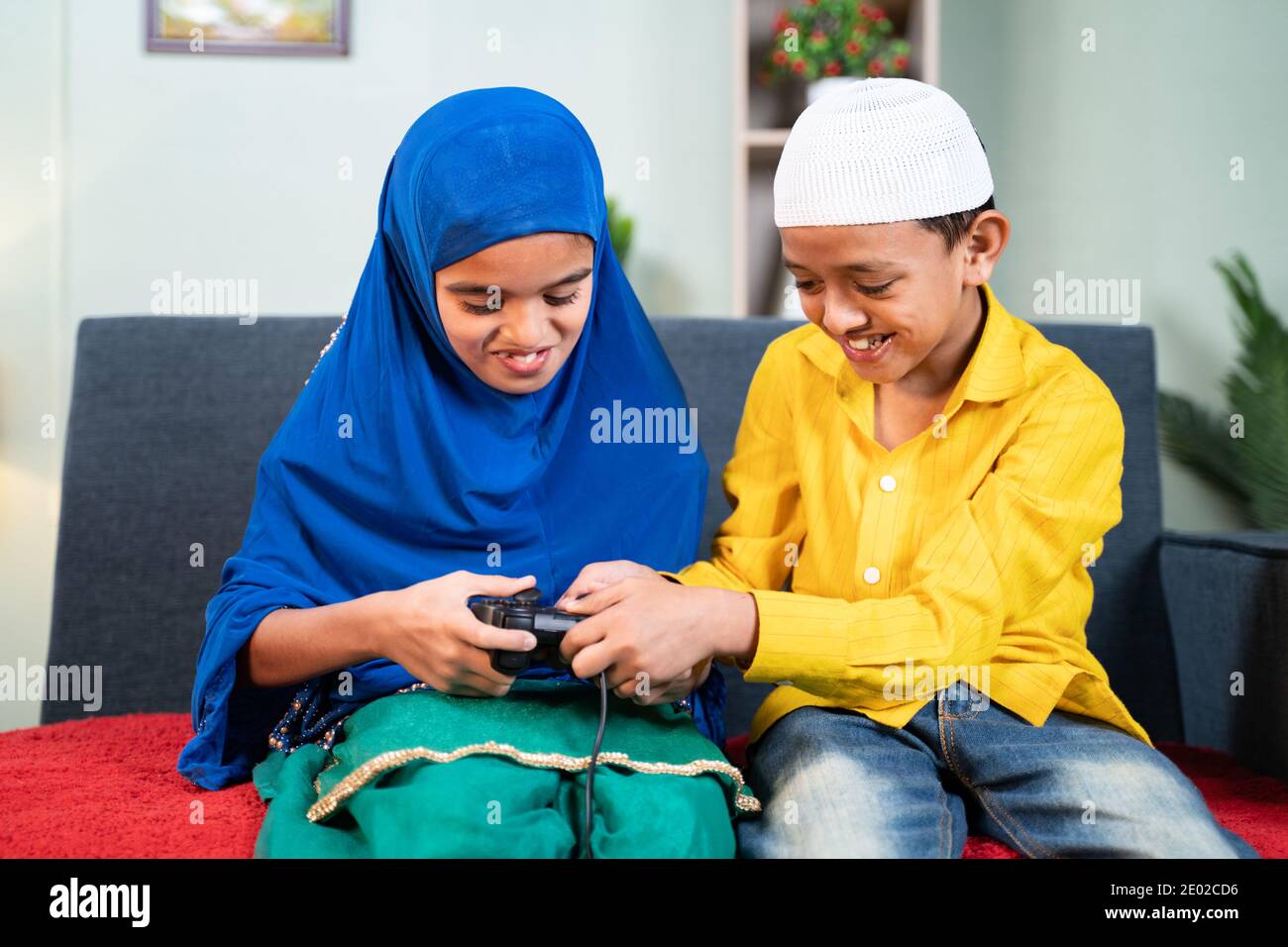 Muslim brother snatching gamepad from his sister to play video game at home - Concept of childhood sibling fighting Stock Photo
