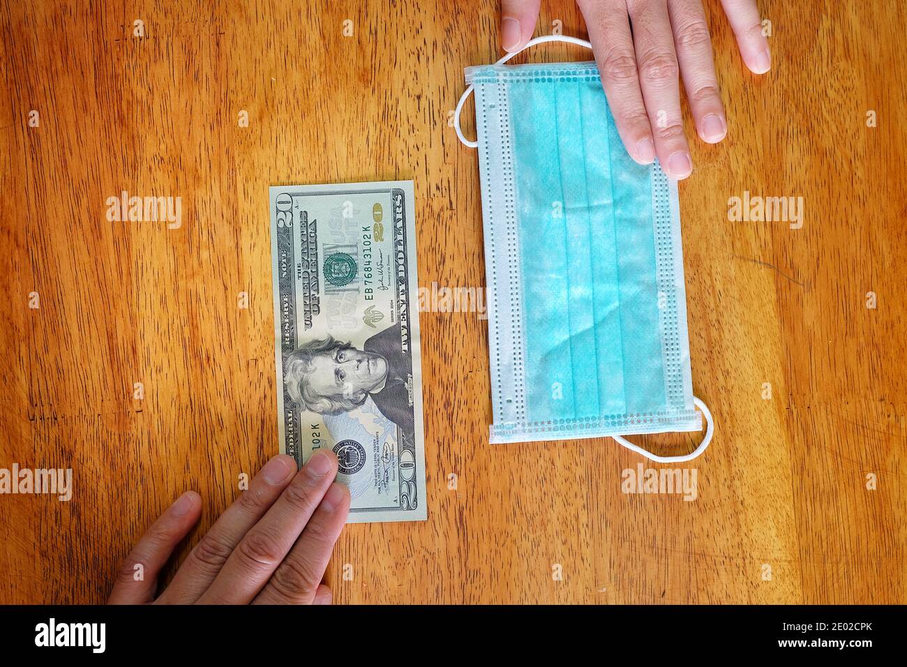 Hands exchanging 20 dollar bill for a surgical face mask signifying a spike in price of face mask during the corona virus pandemic of 2020. Stock Photo