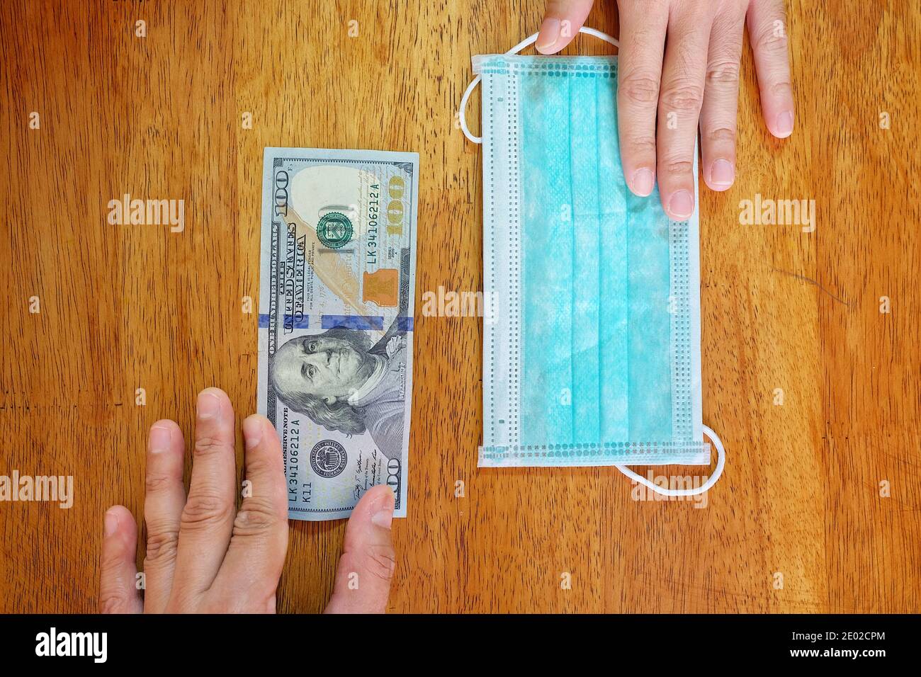 Hands exchanging 100 dollar bill for a surgical face mask signifying a spike in price of face mask during the corona virus pandemic of 2020. Stock Photo