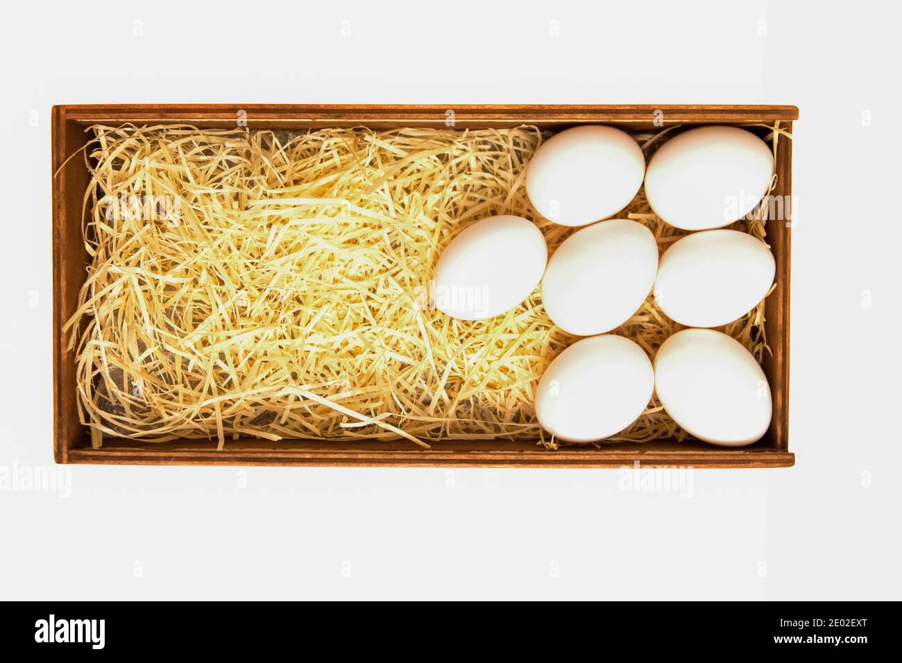 White chicken eggs lie on straw in a wooden box, isolated on a white ...
