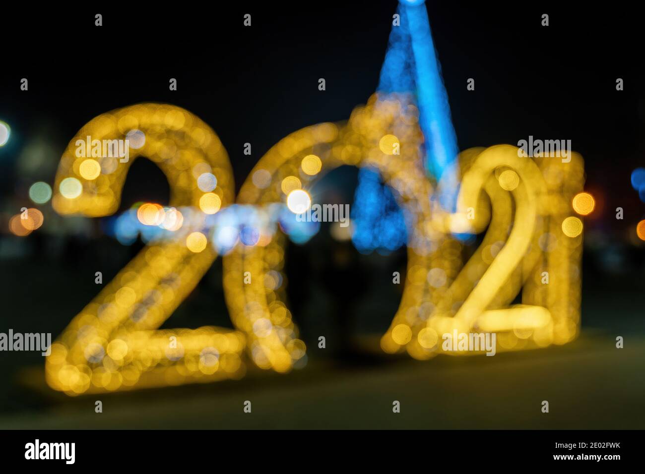 Defocused silhouettes of big golden 2021 figures New Years holiday lights. Blurry street New Year's light installation. Lighting decoration for the Stock Photo