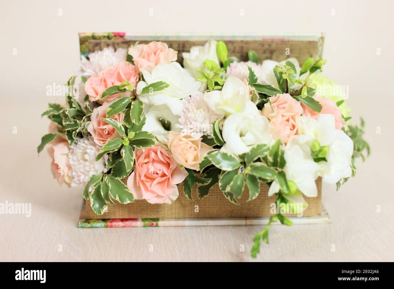 Flower box with white freesia, peach roses, light greens. Fluffy, floral birthday present or other celebration. Stock Photo