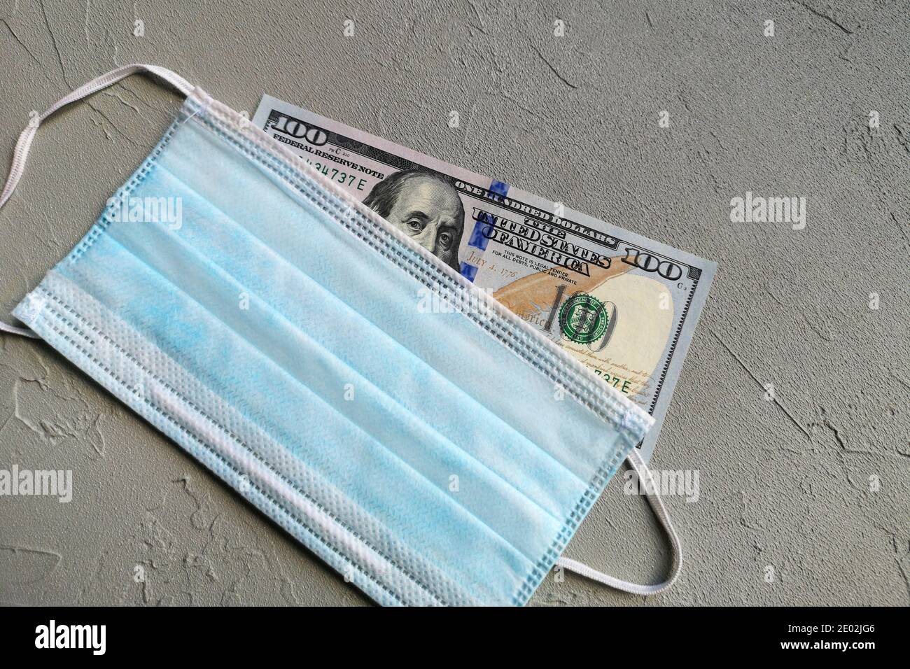 One hundred dollar bill and blue medical masks on gray table. Stock Photo