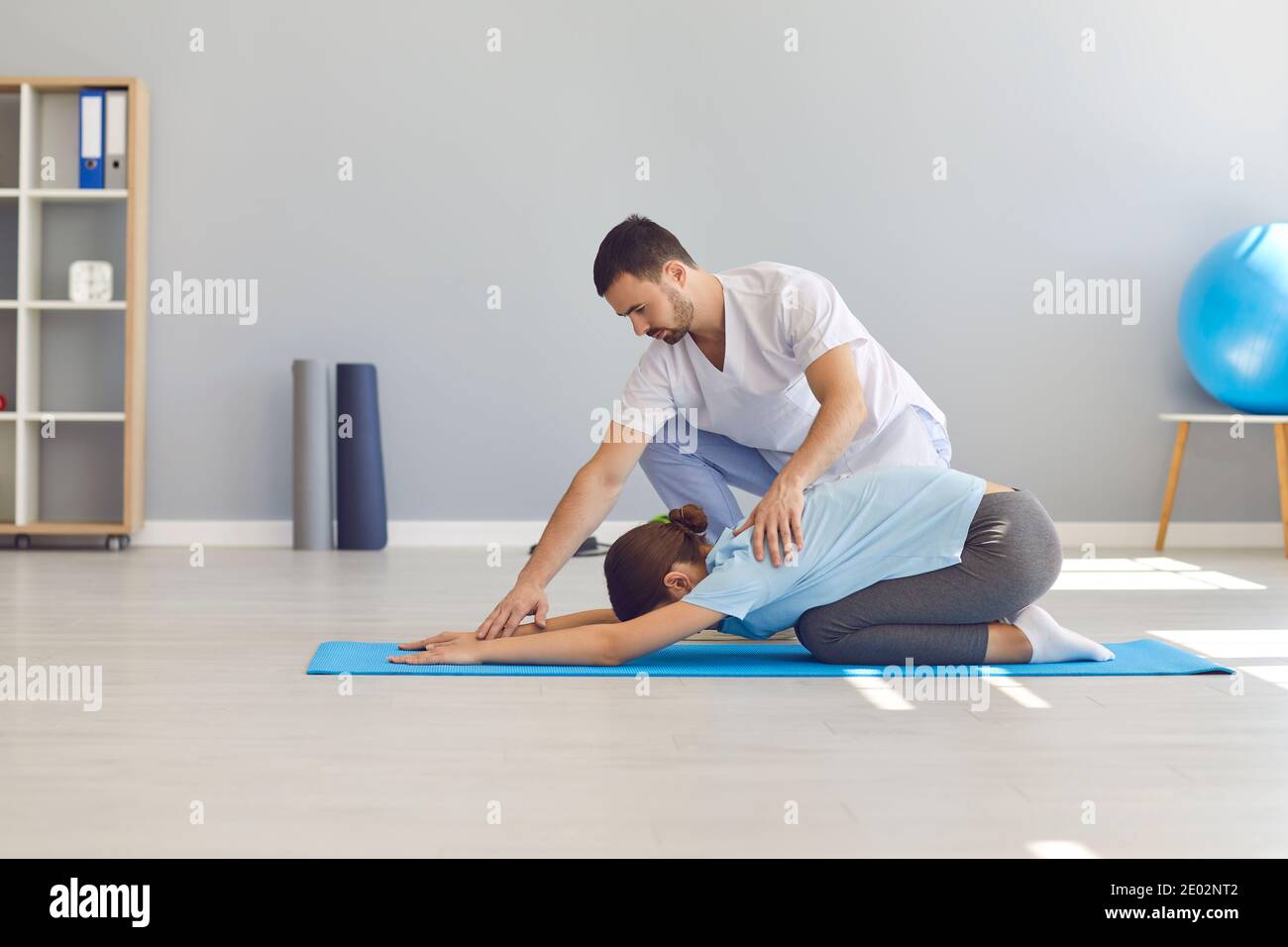 Side view the doctor helps the woman to do stretching and yoga exercises after the injury. Stock Photo