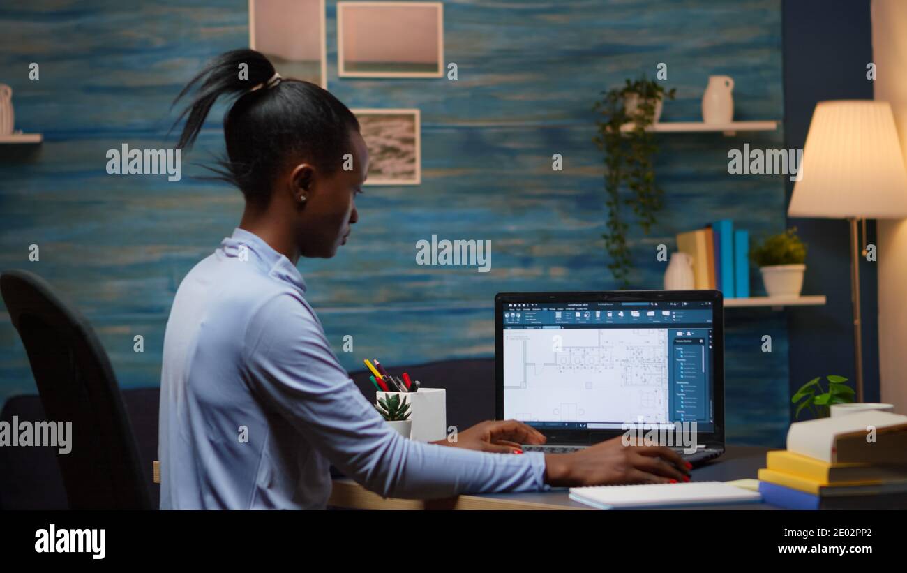 African freelancer analysing digital blue prints checking project of company looking on laptop sitting at desk in living room office late at night overtime. Busy black employee using modern technology Stock Photo