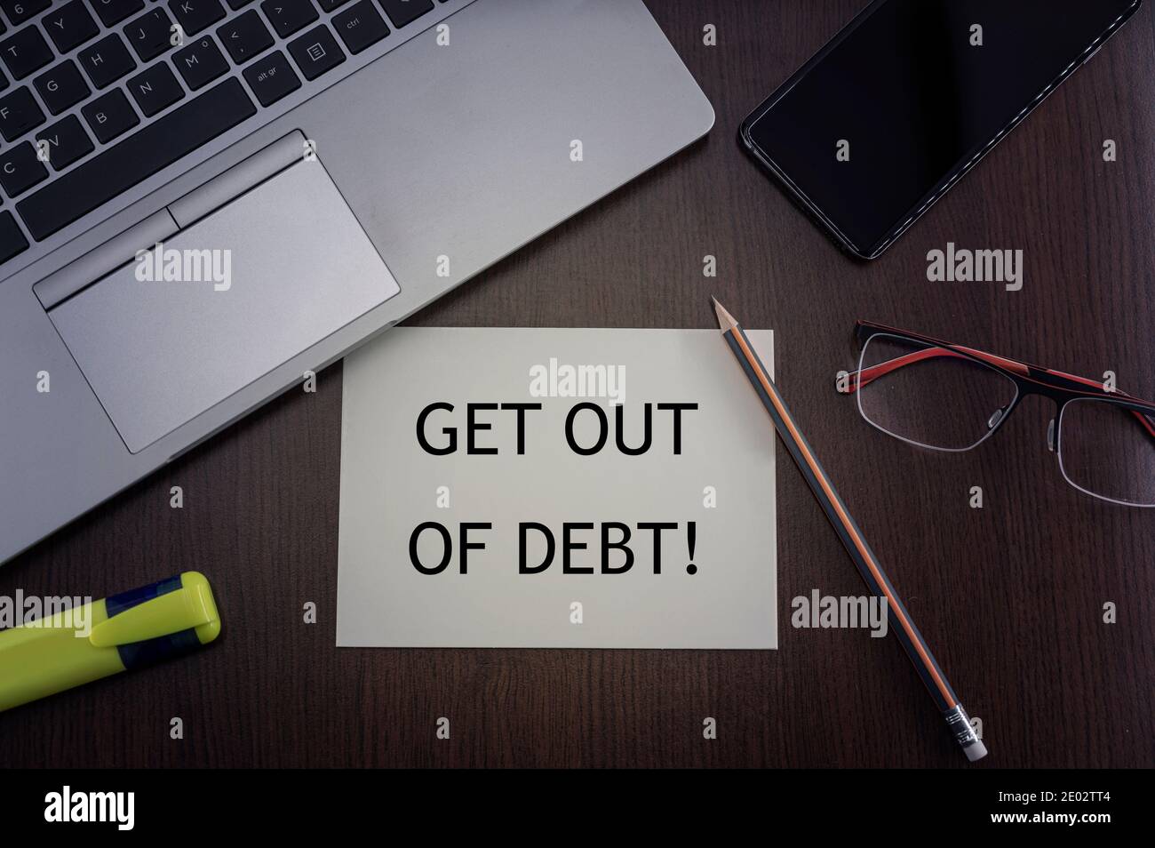 Get out of debt card. Top view of office table desktop background with laptop, phone, glasses and pencil with card with inscription get out of debt. Stock Photo