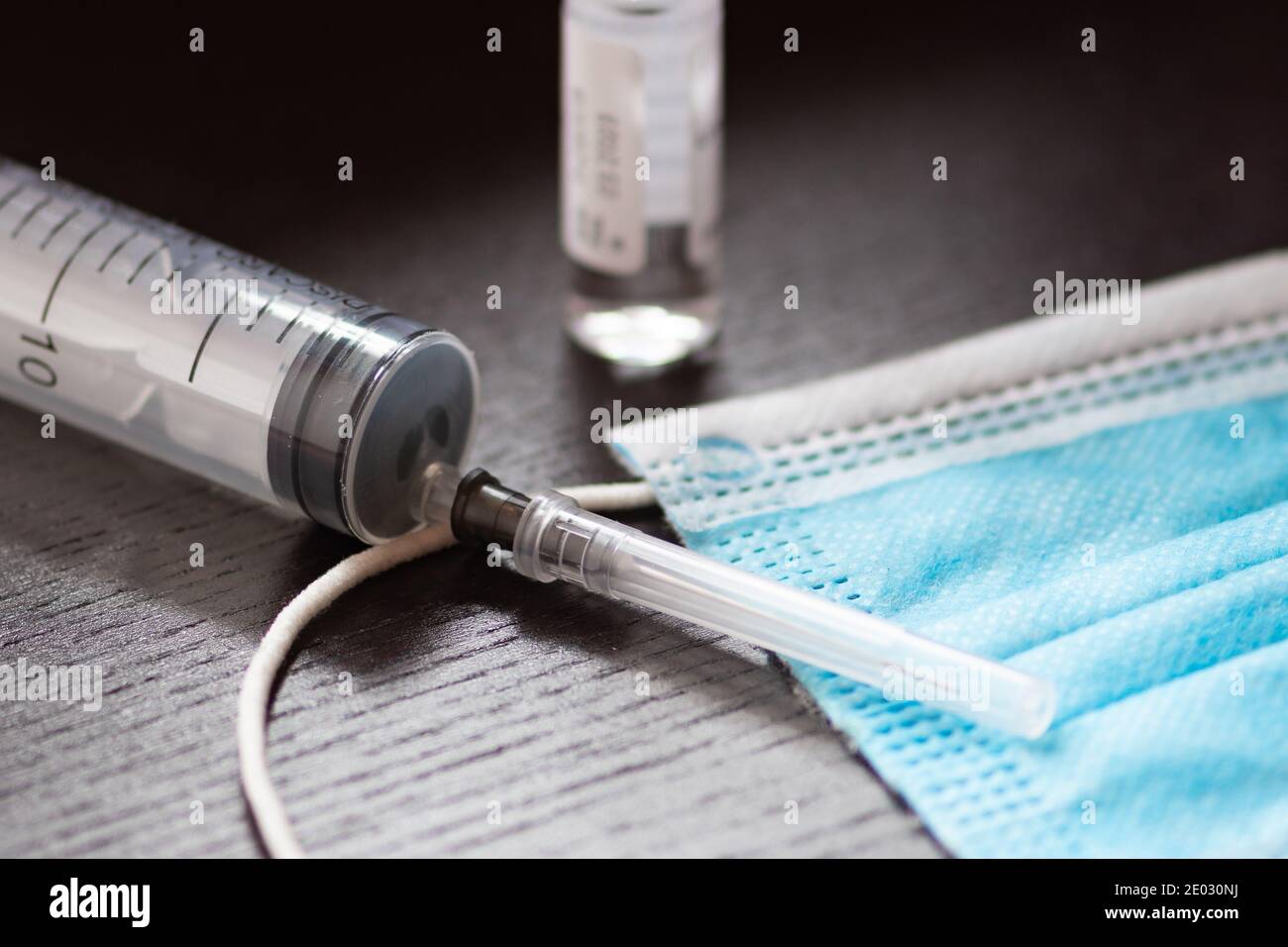 Syringe, vial and surgical face mask on a black table. Covid or Coronavirus vaccine background Stock Photo