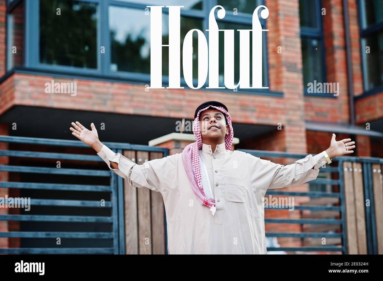 Hofuf - biggest city of Saudi Arabia. Middle Eastern saudi arabian man posed on street against modern building up his hands in the air. Stock Photo