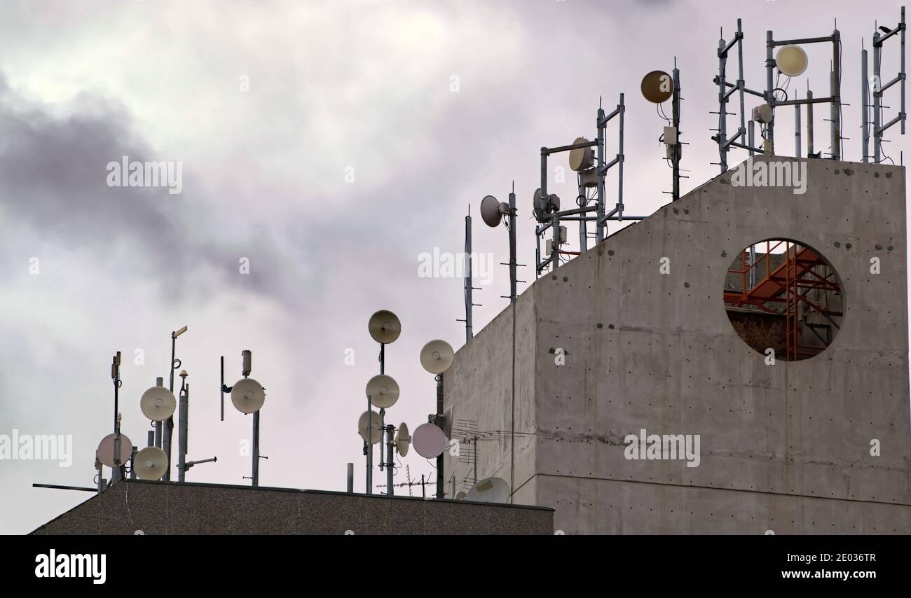 Numerous communication dishes and antennae on concrete roof Stock Photo