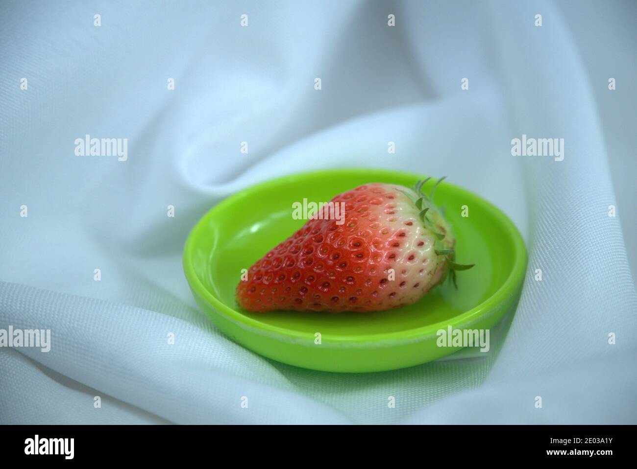Closeup of a fresh ripe strawberry isolated on a small green tray. Blue ...