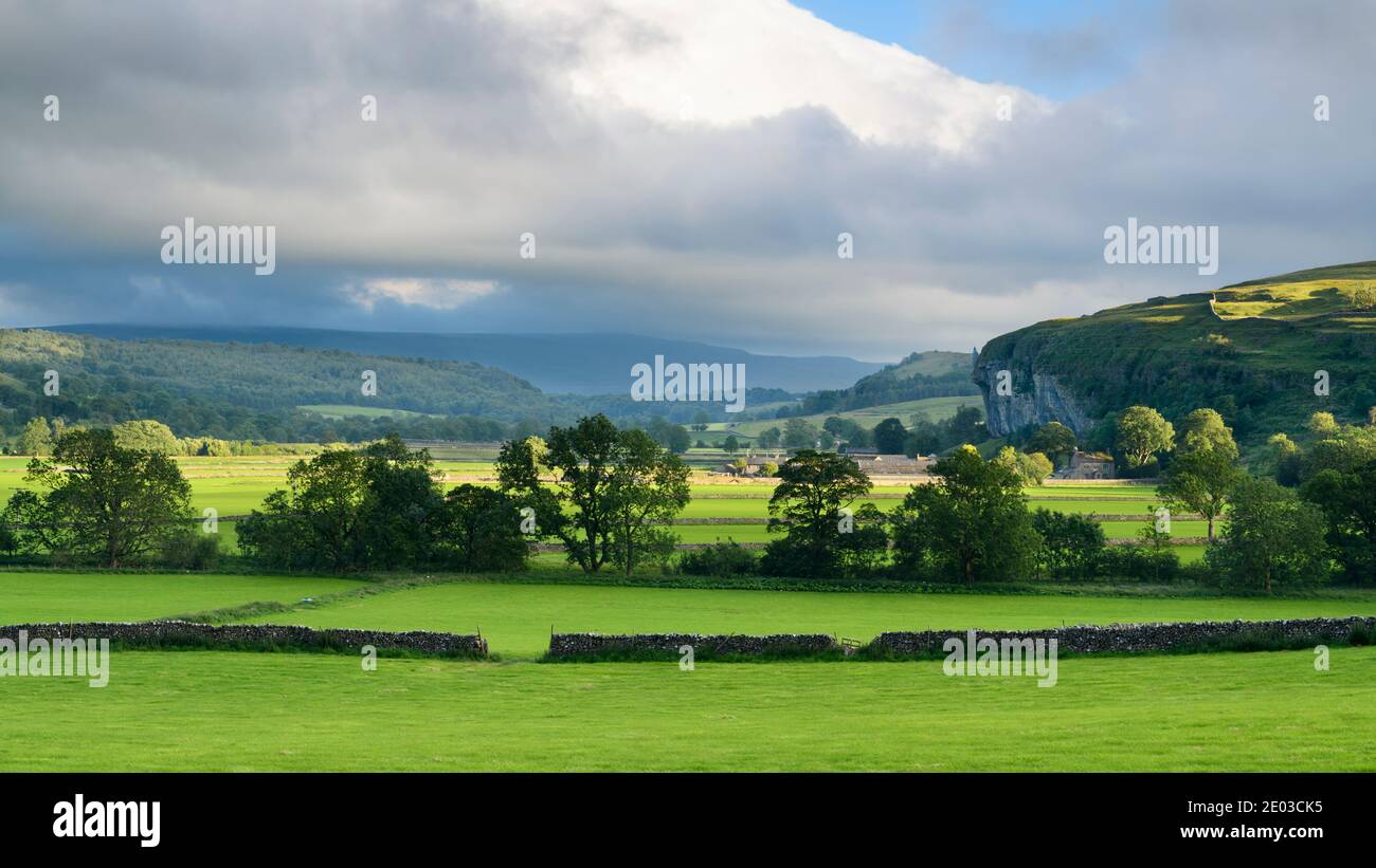 Scenic Wharfe Valley (flat sunlit fields, stone walls, Kilnsey Crag - high limestone cliff, rolling hills) - Wharfedale, Yorkshire Dales, England, UK. Stock Photo