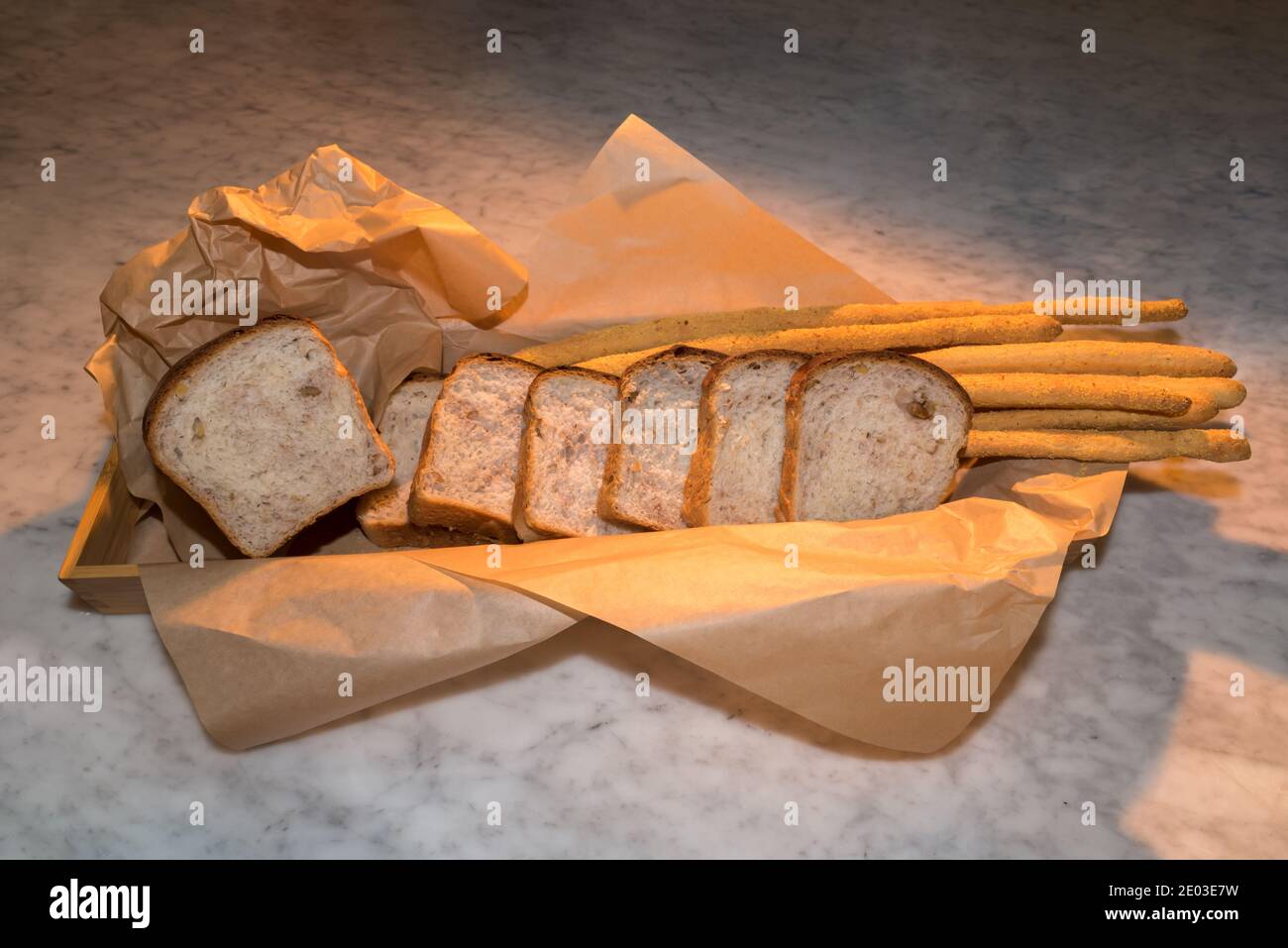 Bread with walnuts, slices of loaf on breadsticks in brown bakery paper on a marble surface Stock Photo