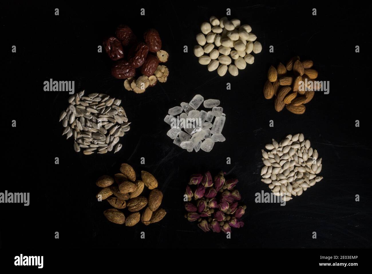 Eight ingredients on black background in flower shape, roses, red dates, rock candies, peanuts, almonds, sunflower seeds and winter melon seeds Stock Photo
