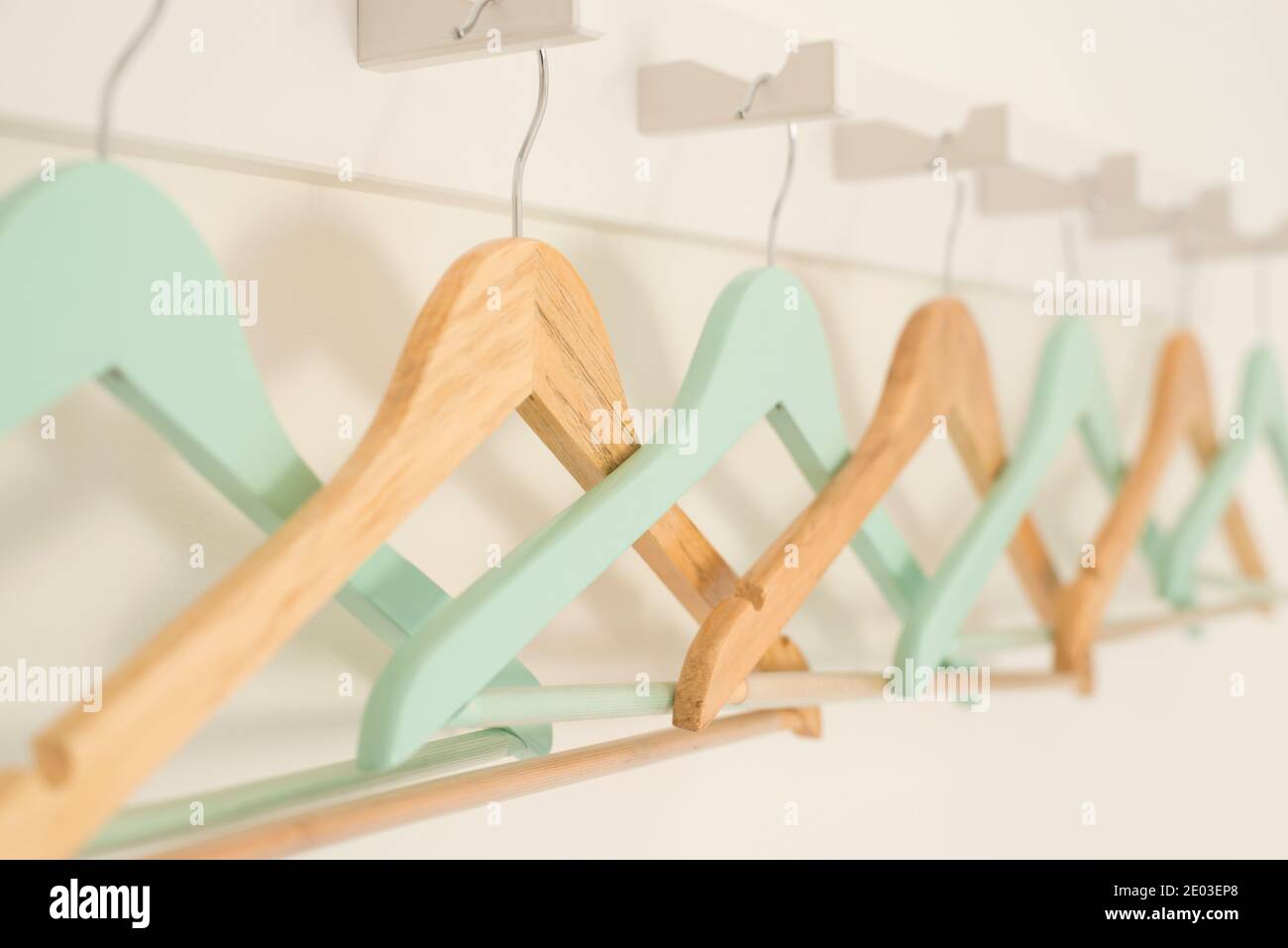 Plain and painted wooden coat hangers hanging from a row of hooks Stock Photo