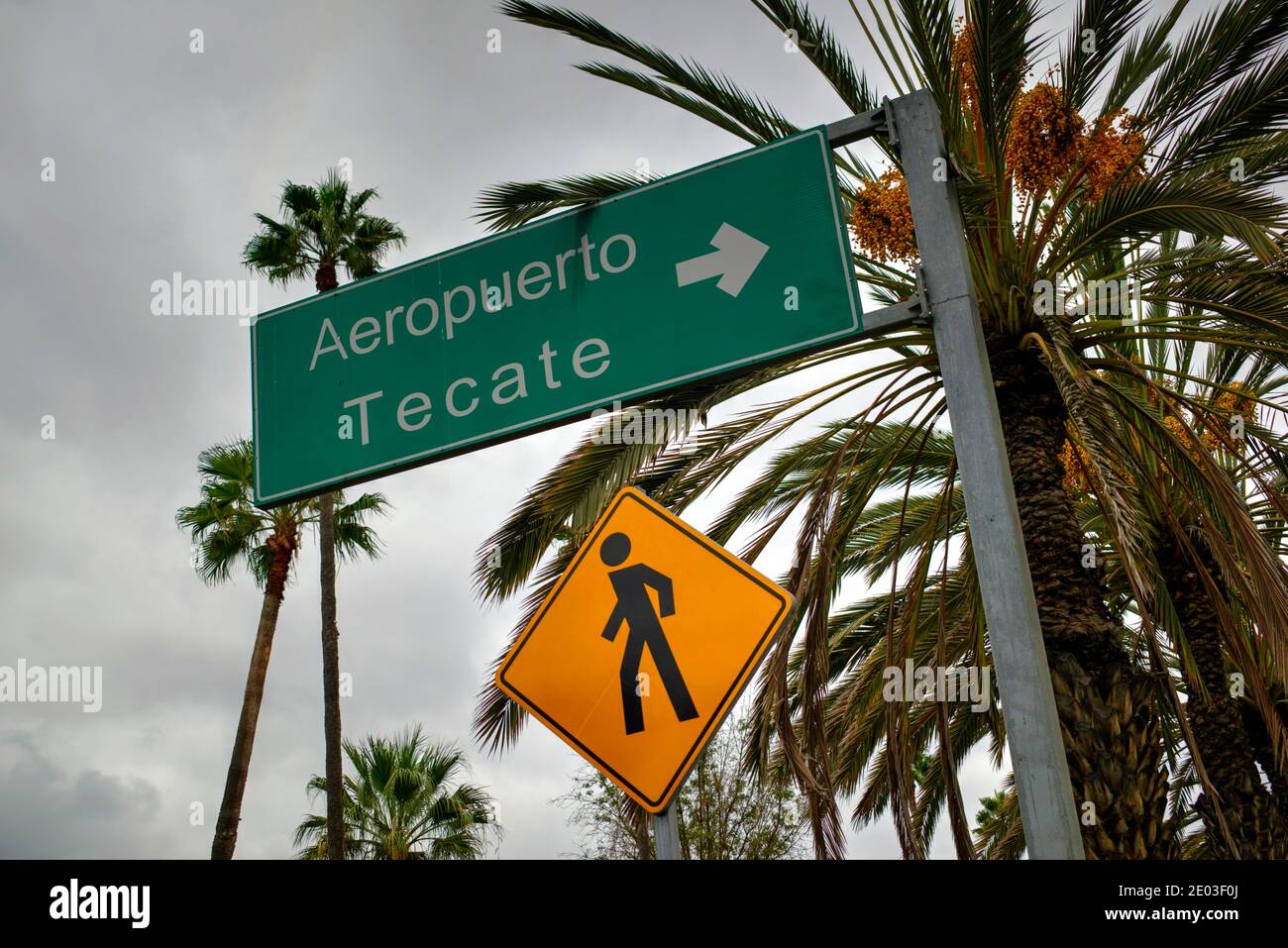 Tijuana, Mexico - October 30, 2017: Yellow diamond shaped pedestrian access sign with green sign indicating direction to Airport Tecate Stock Photo