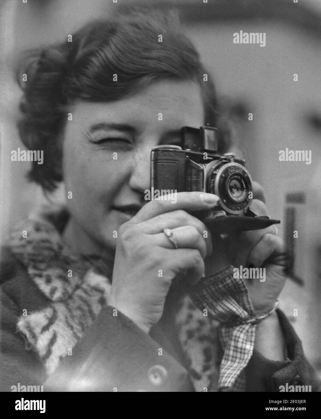 1930s, historical, a young lady closing her eyes to focus as she takes a photograph with a 'Nagel'  Vollenda folding compact film camera. Formed by Dr. August Nagel, co-founder of Zeiss Ikon, in Stuggart, Germany in 1928, the company became known for its small format camera Nagel-Pupille. The camera used here is a Vollenda 48, a compact folding camera that producd 16 exposures on 127 film. It had a folding optical viewfinder. Stock Photo