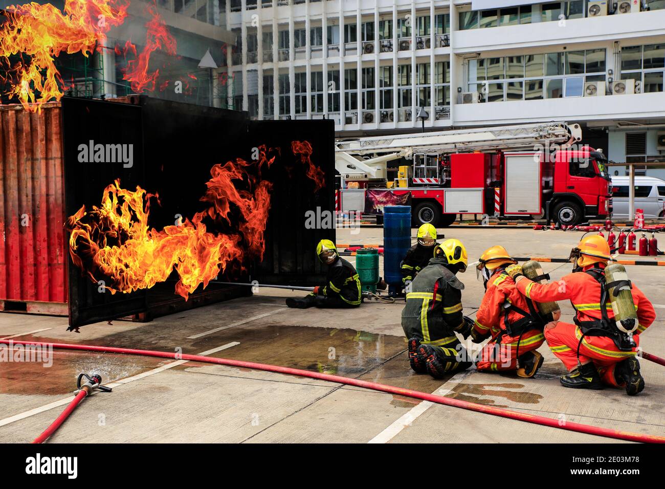 Brave firefighter using extinguisher and water from hose for fire fighting, Firefighter training with protective wear spraying high pressure water to Stock Photo