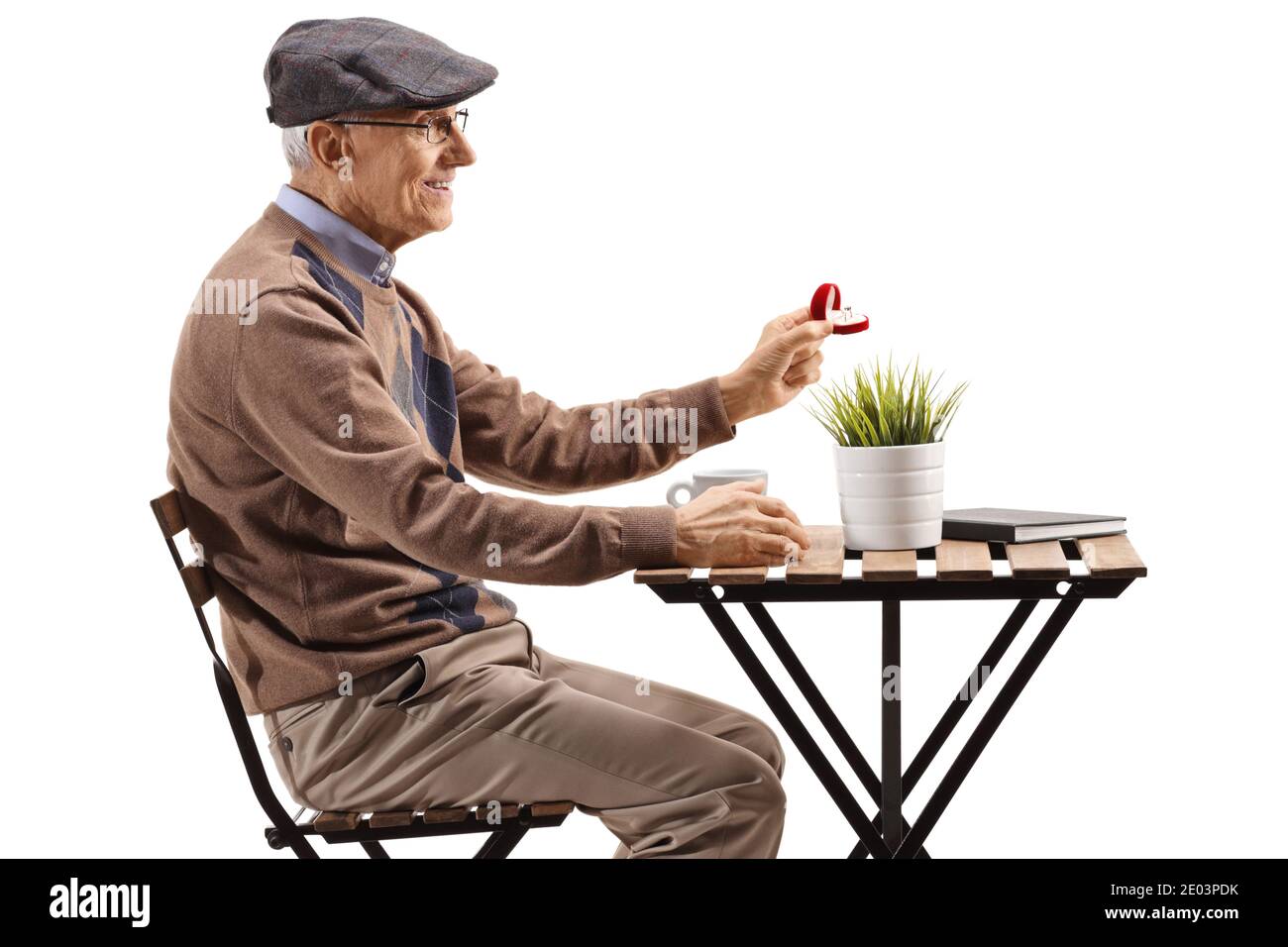 Elderly man sitting at a cafe and holding a ring in a box isolated on white background Stock Photo