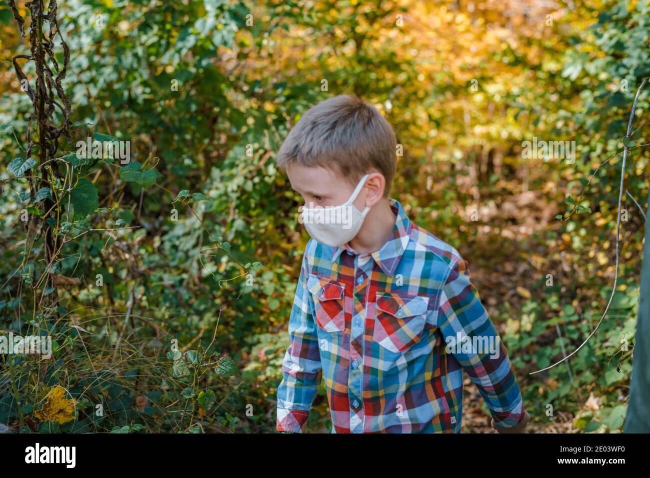 Young boy walking in woods wearing protective face mask Stock Photo