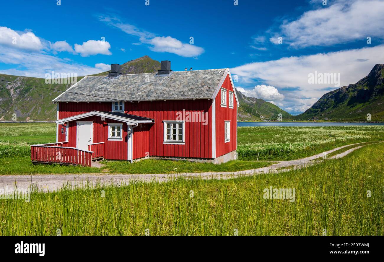 Vaeroy Island Lofoten Islands Nordland Norway Red house in green meadows with blue sky with white clouds in summer in Norway Stock Photo