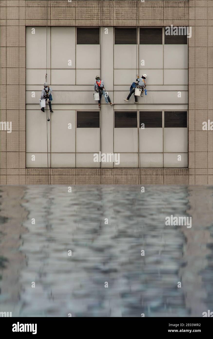 Group of workers cleaning windows service on high rise office building with reflection fiom swimming pool. Selective focus. Stock Photo