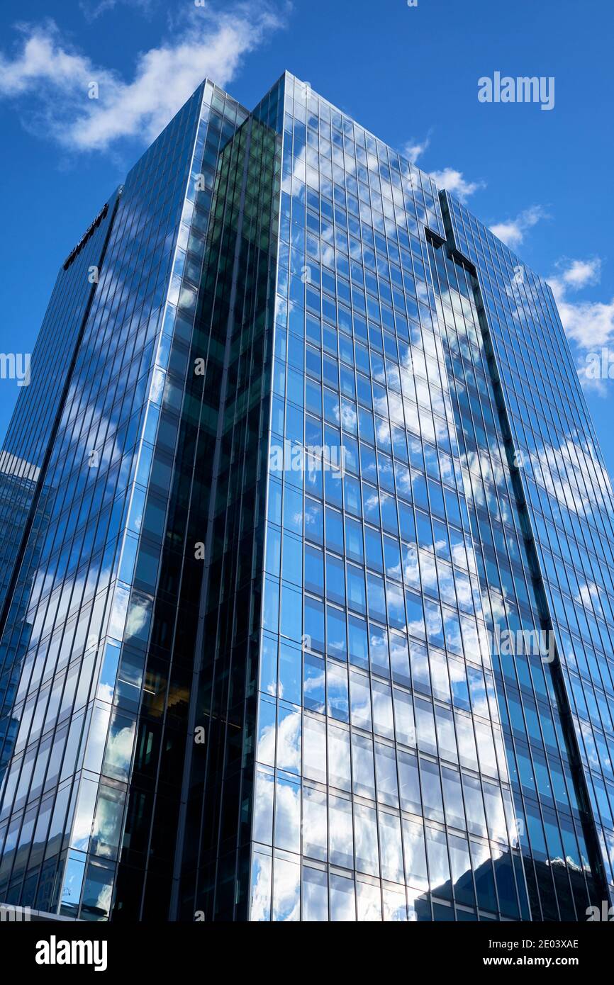 A modern glass office building reflects clouds on a blue sky background ...