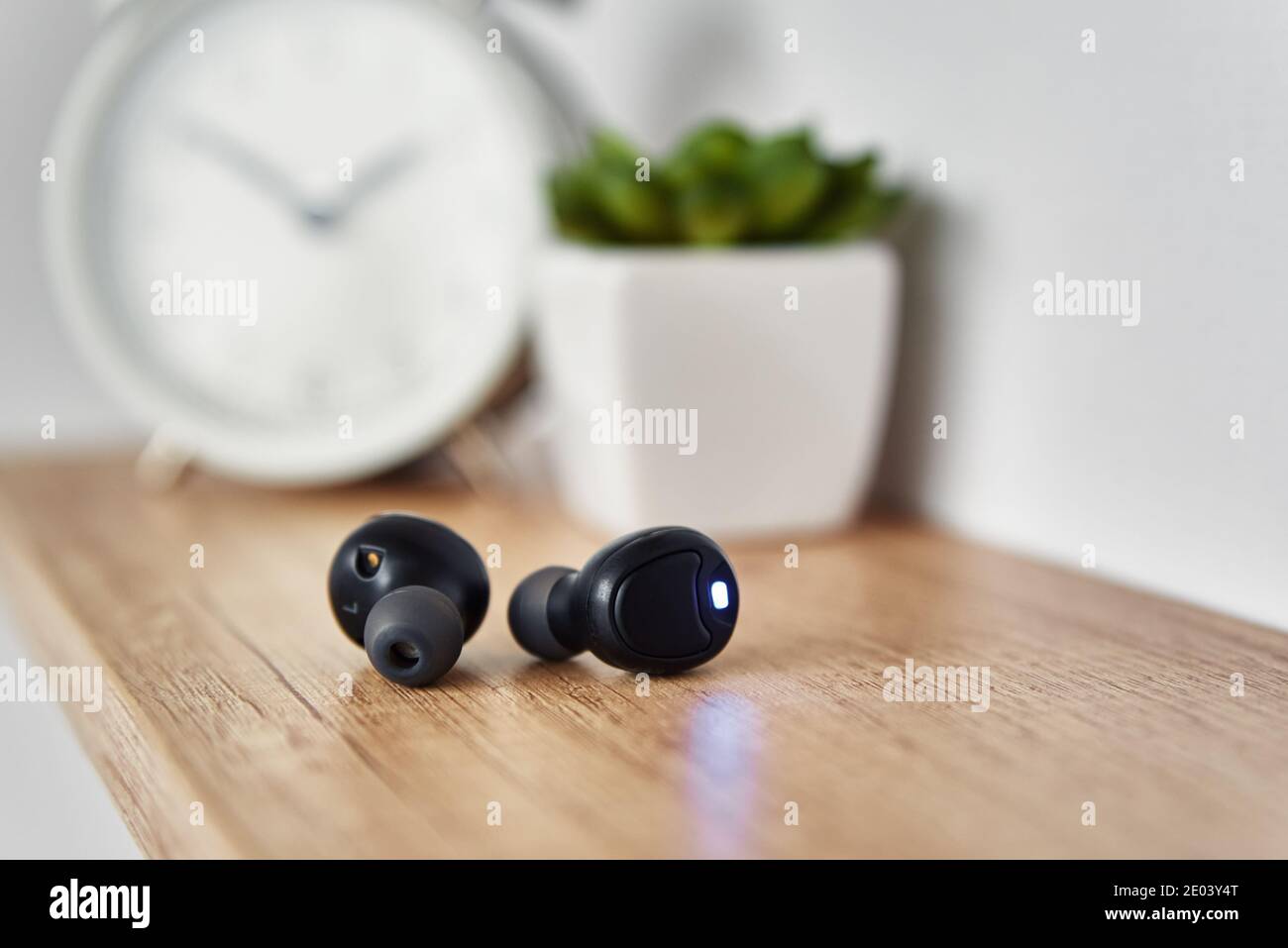 Wireless earphones on the shelf with alarm clock and house plant. Headphones  in home office interior Stock Photo - Alamy