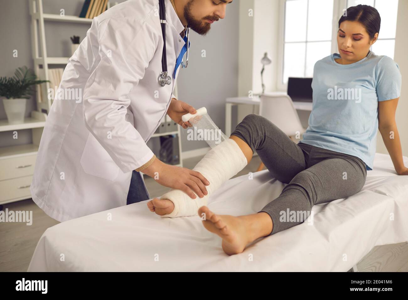 Doctor at the injury care center provides first aid to young woman with leg bone fracture Stock Photo