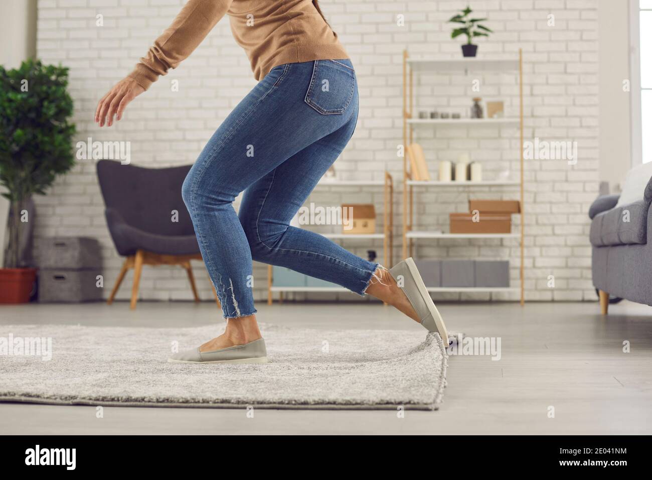 Clumsy woman trips over the rug in the living-room and is about to fall on the floor Stock Photo