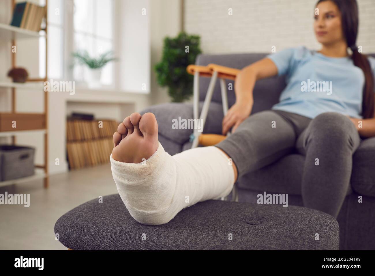 Young woman with broken leg resting on sofa during rehabilitation